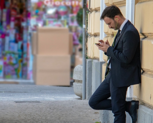 Business suited man with ear plugs looking at his phone outside
