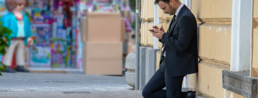 Business suited man with ear plugs looking at his phone outside